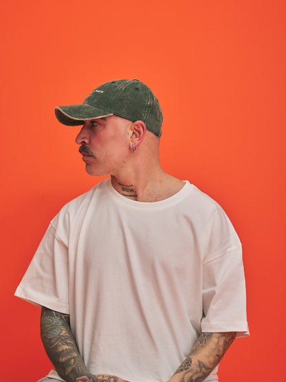 Man wearing a green cap and white t-shirt against an orange background