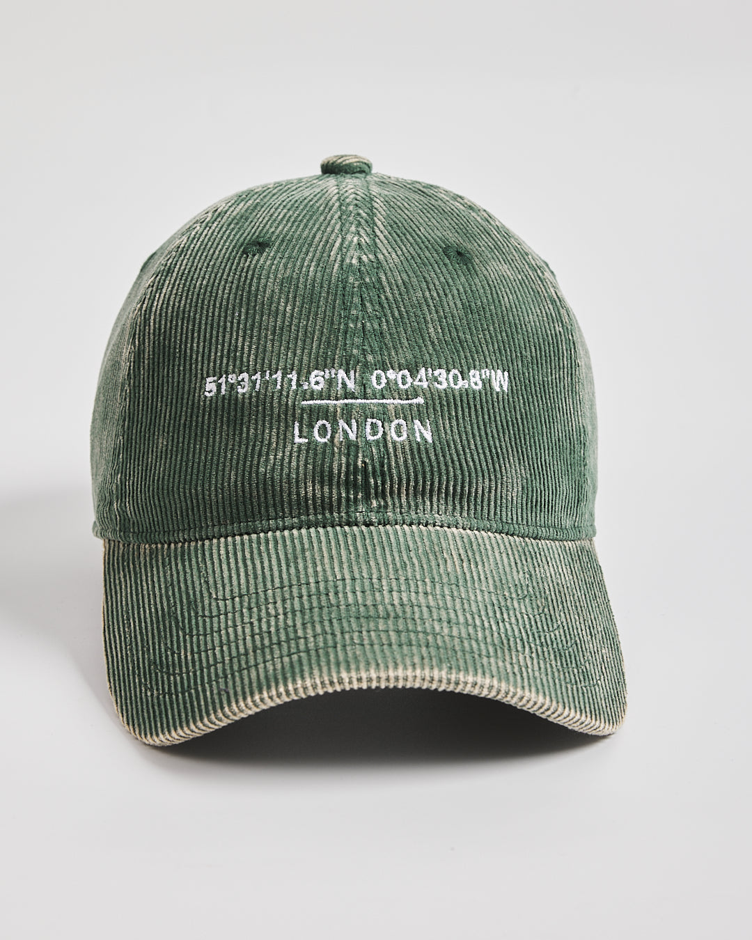 Green corduroy cap with embroidered text on a light gray background