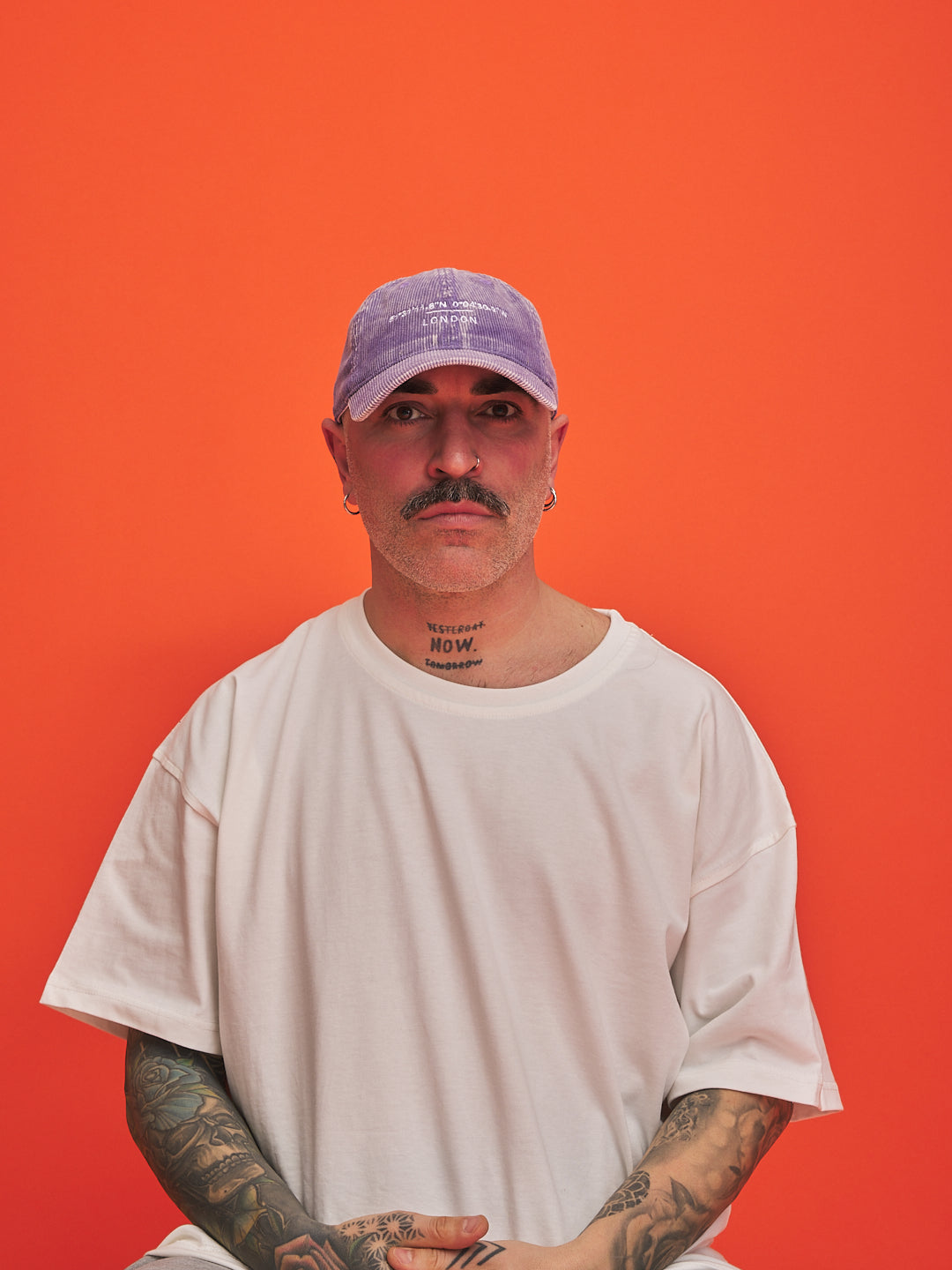Man wearing a white t-shirt and purple cap against an orange background