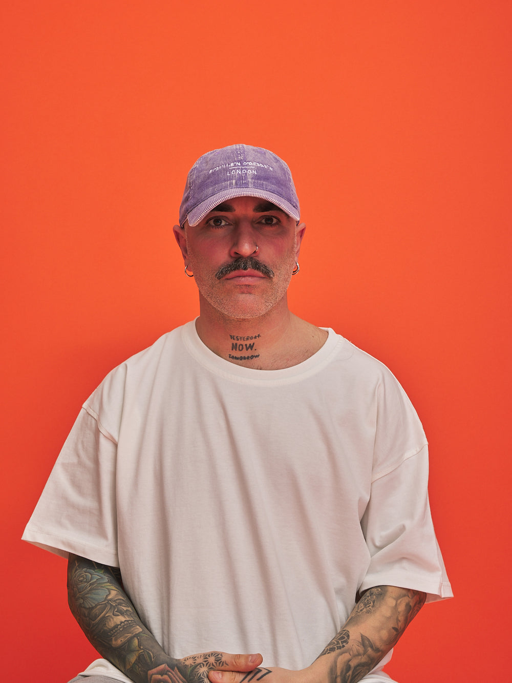 Man wearing a white t-shirt and purple cap against an orange background