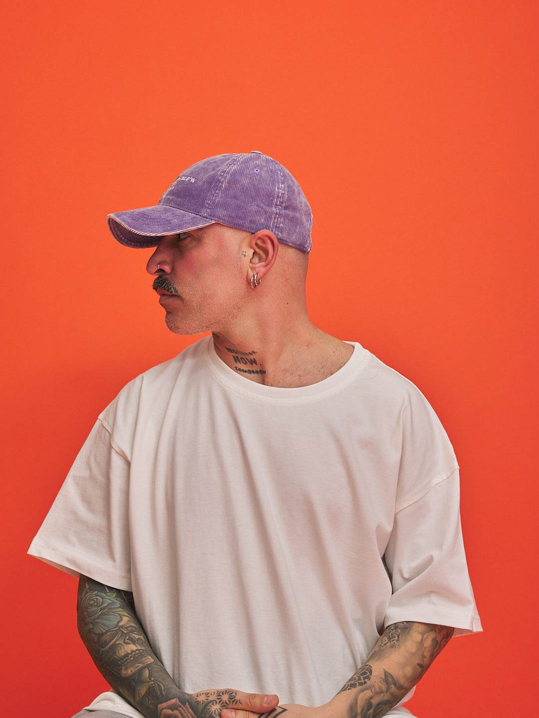 Person wearing a purple cap and white t-shirt against an orange background
