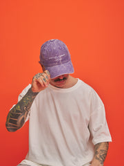 Person wearing a purple cap and white t-shirt against an orange background