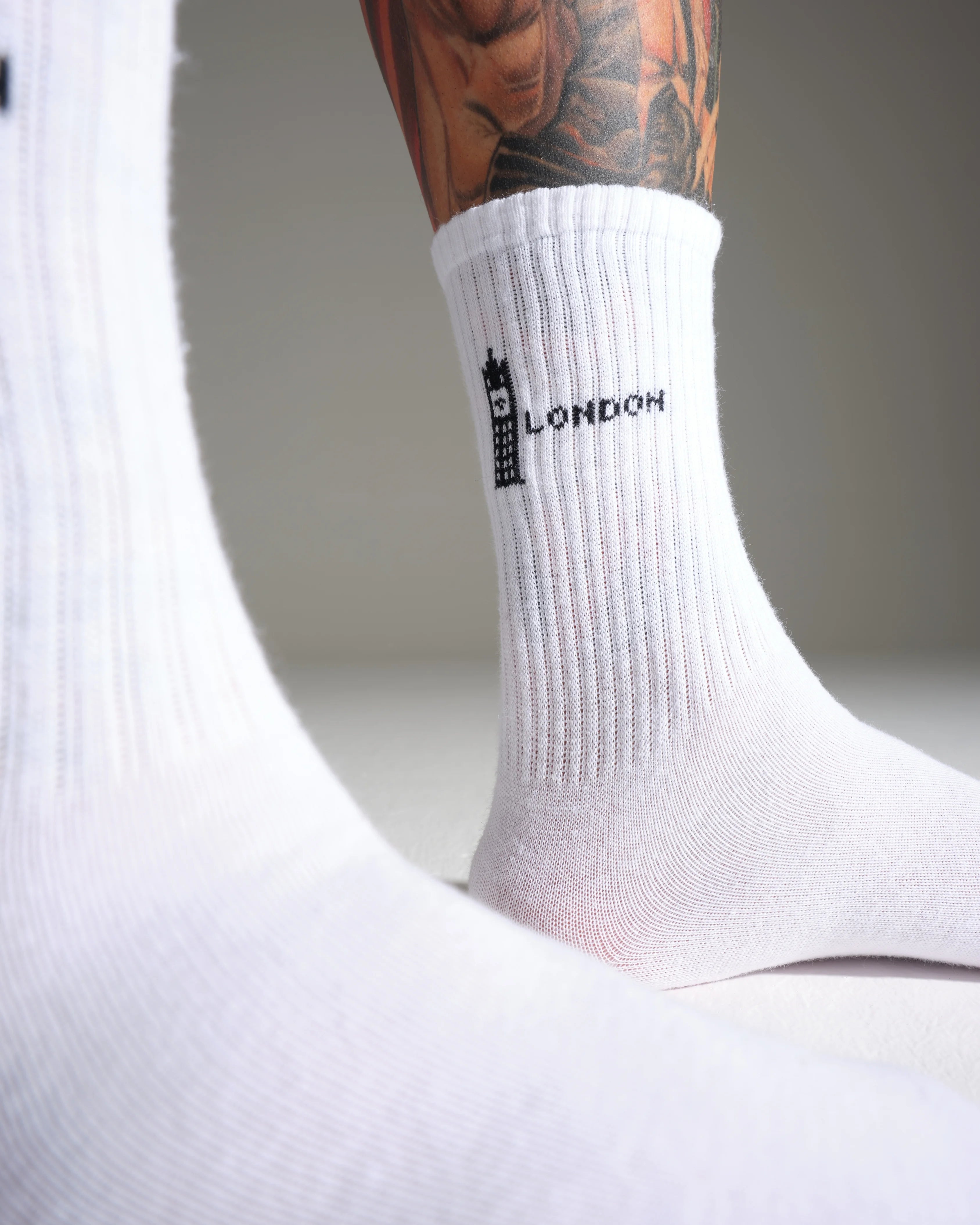 White sock with 'London' text and Bigben logo worn by a person with tattoos.