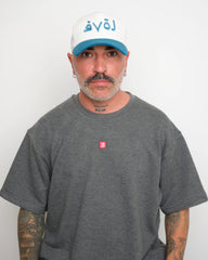 Man wearing a gray t-shirt with a small red VELO logo and a white cap with blue brim and blue Arabic 'love' text on a plain background