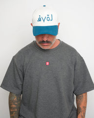 Man wearing a gray t-shirt with a small red VELO logo and a white cap with blue brim and blue Arabic 'love' text on a plain background
