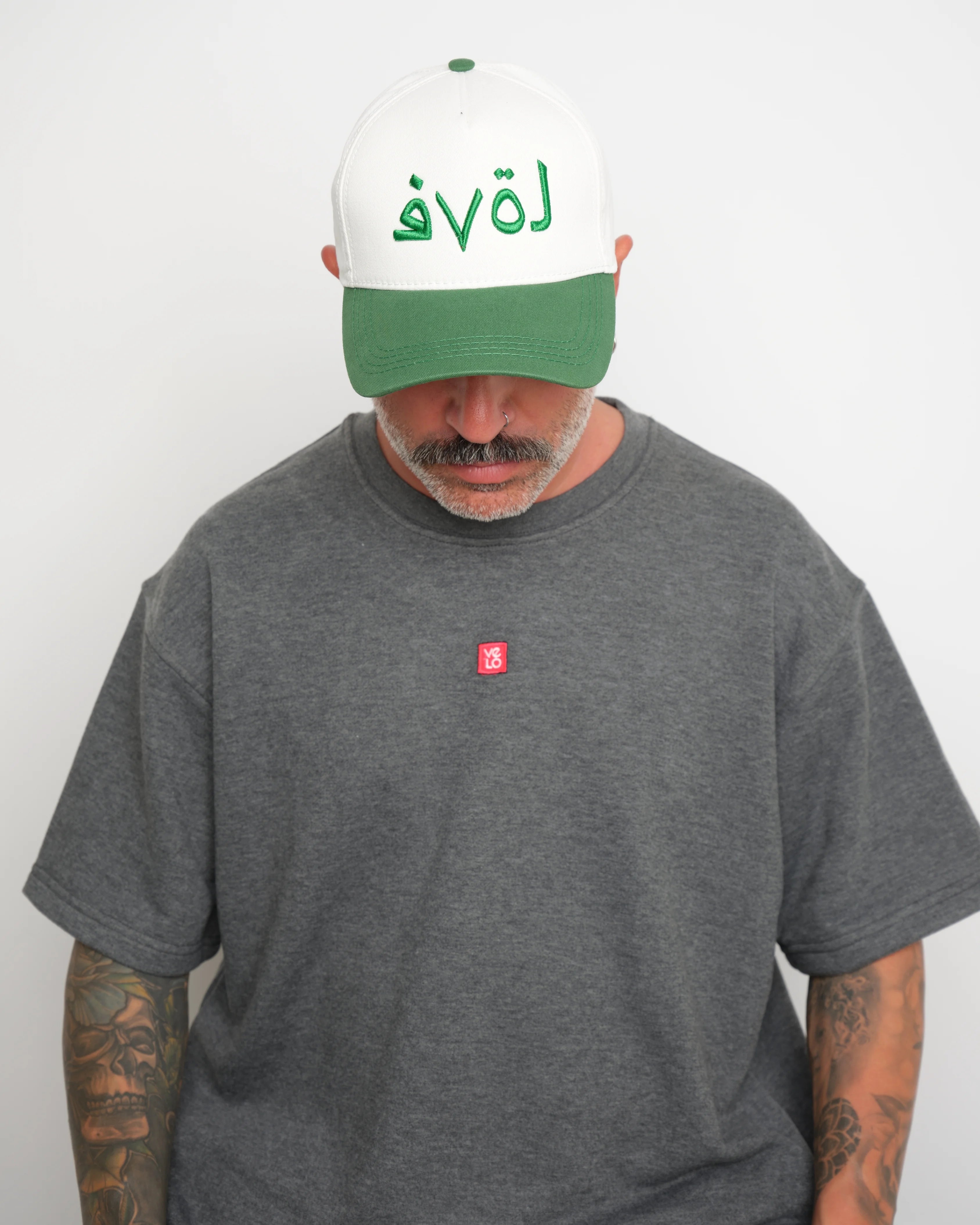 Man wearing a gray t-shirt with a small red logo and a white cap with green brim and green 'love' text.
