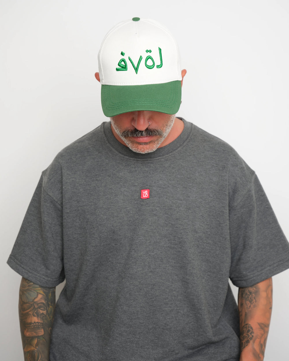 Man wearing a gray t-shirt with a small red logo and a white cap with green brim and green 'love' text.