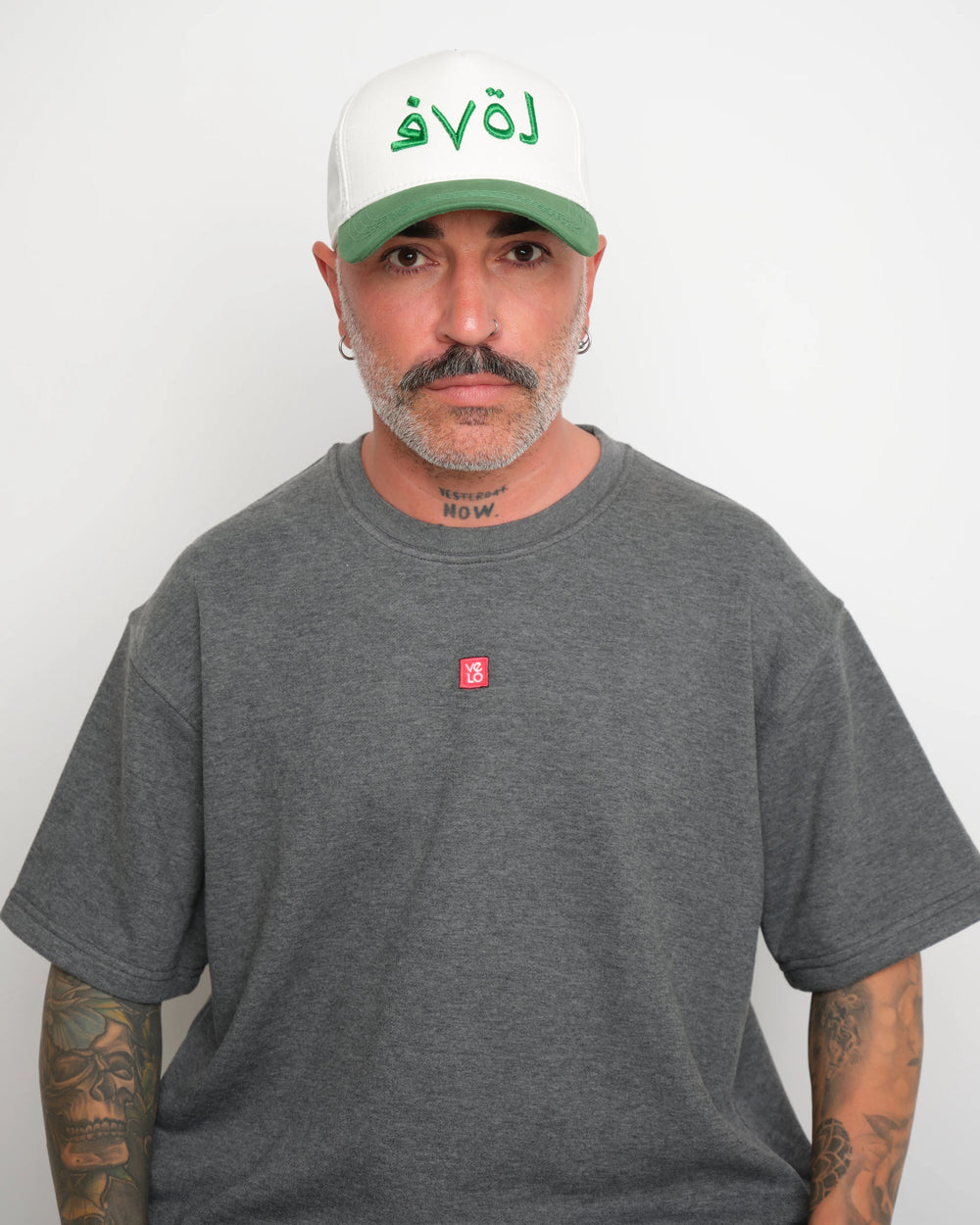 Man wearing a gray t-shirt and white cap with green 'love' text against a plain background