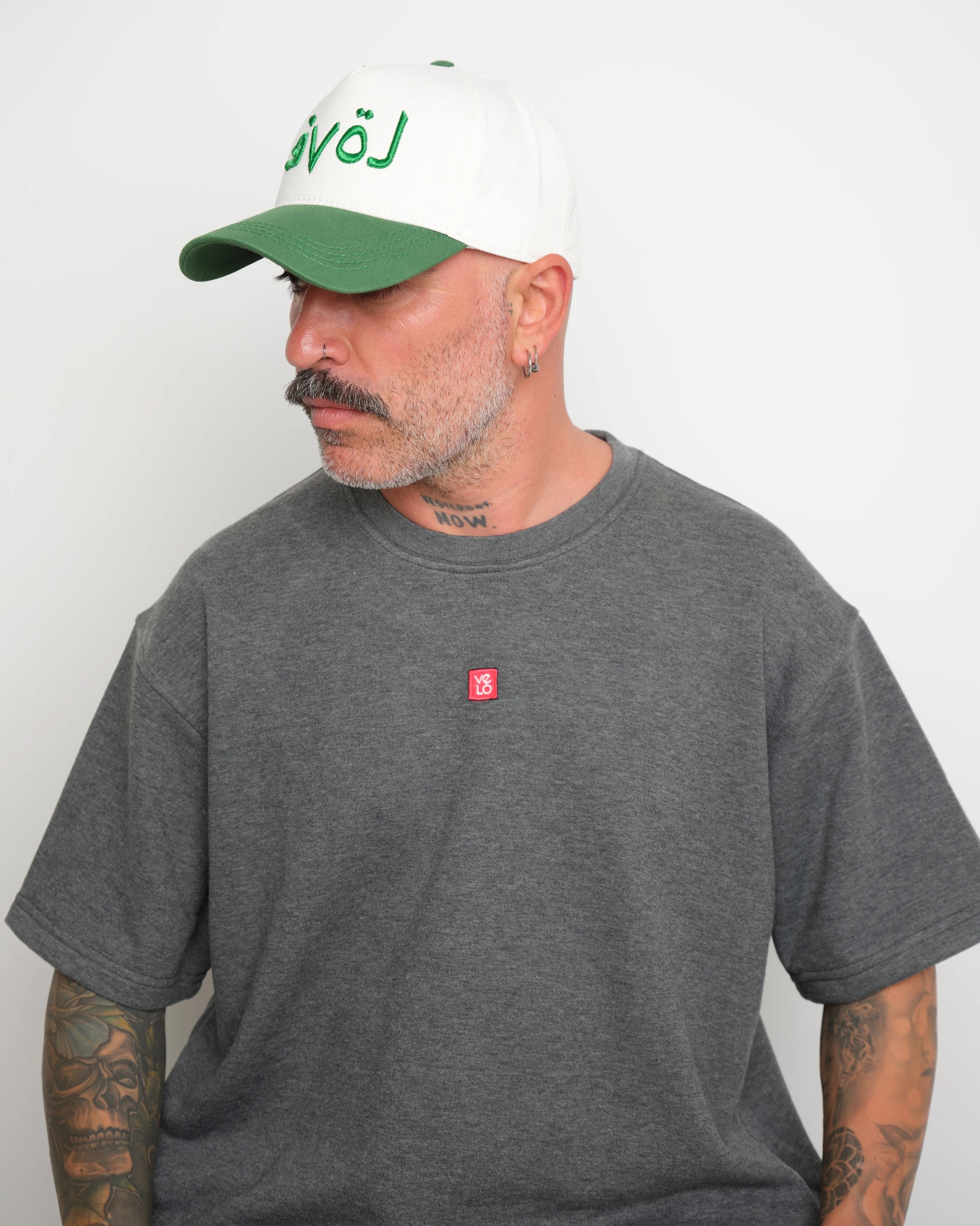 Side of man wearing a gray t-shirt with a small red logo and a white cap with green brim and green 'love' text.