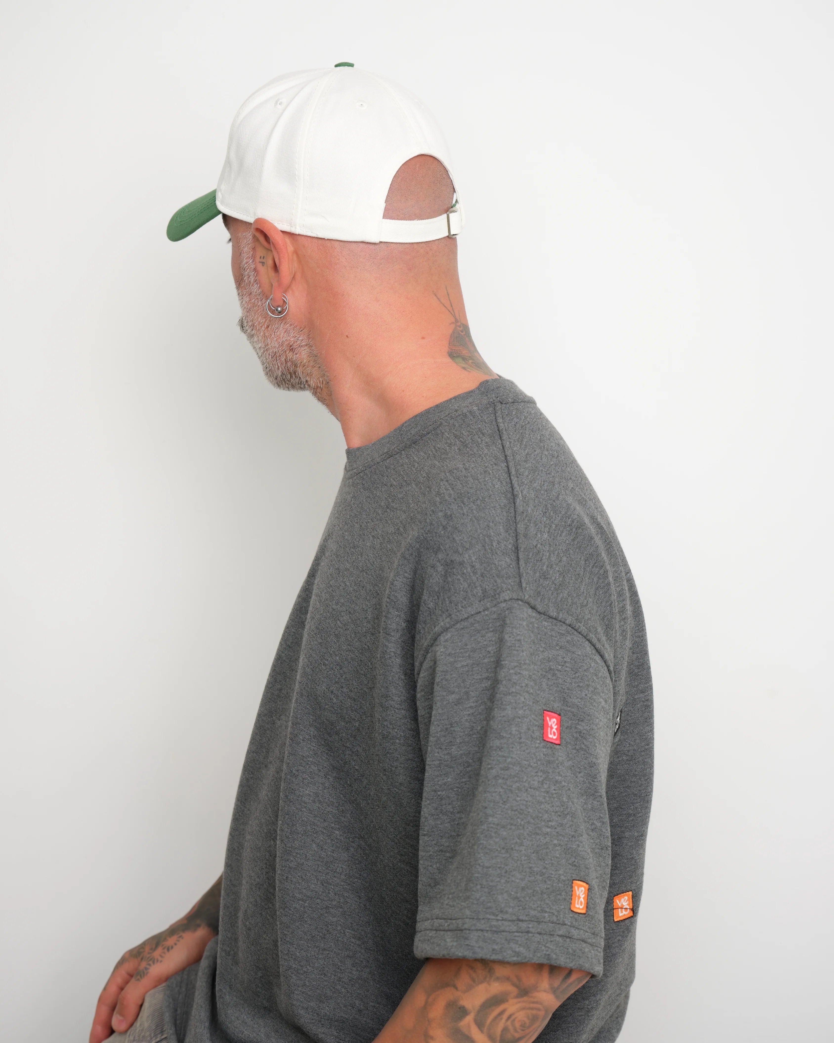 man wearing a gray t-shirt with brand logos and shows adjustable fit of white cap cap with red brim on a white background