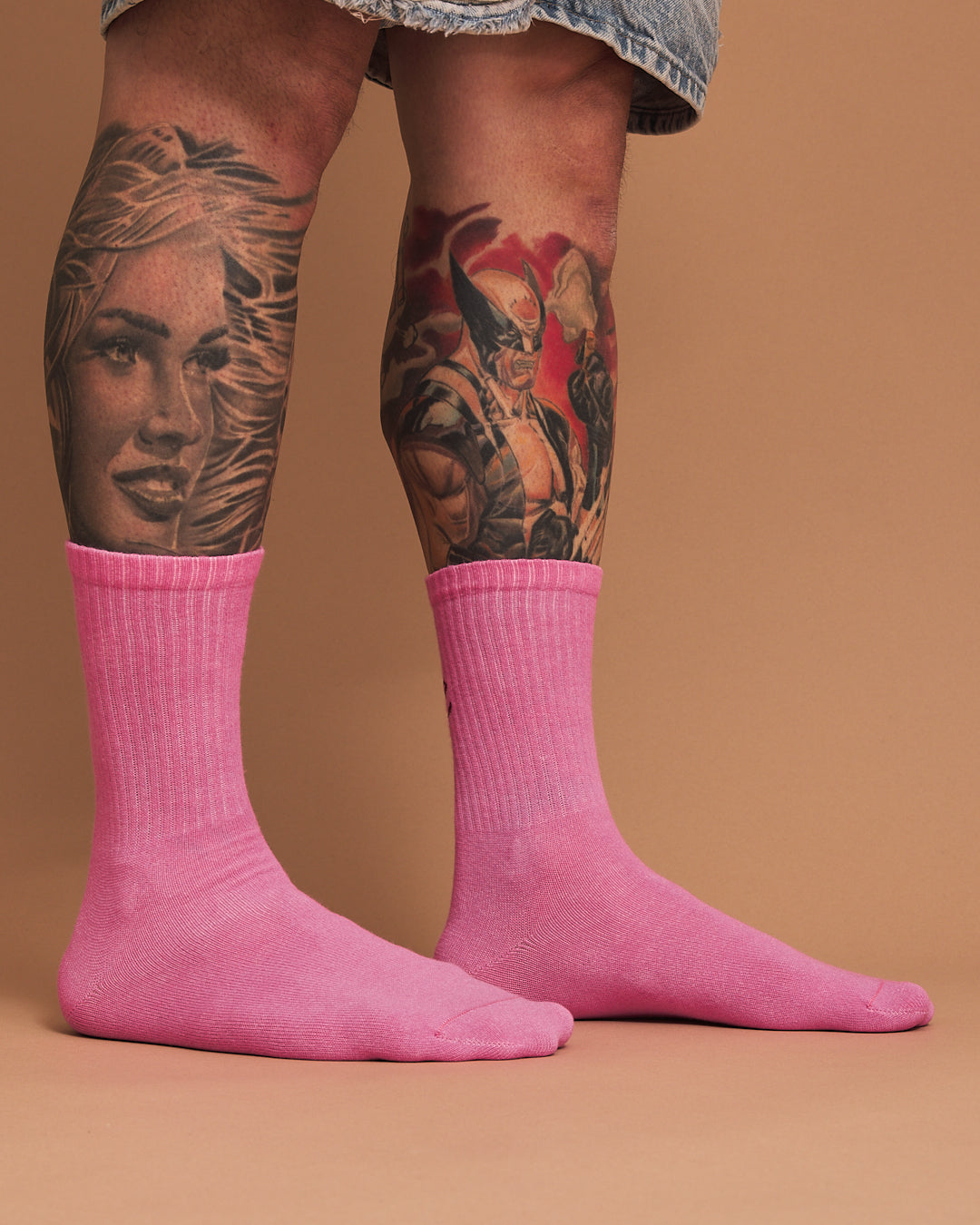 Person wearing pink socks with tattoos on a brown background
