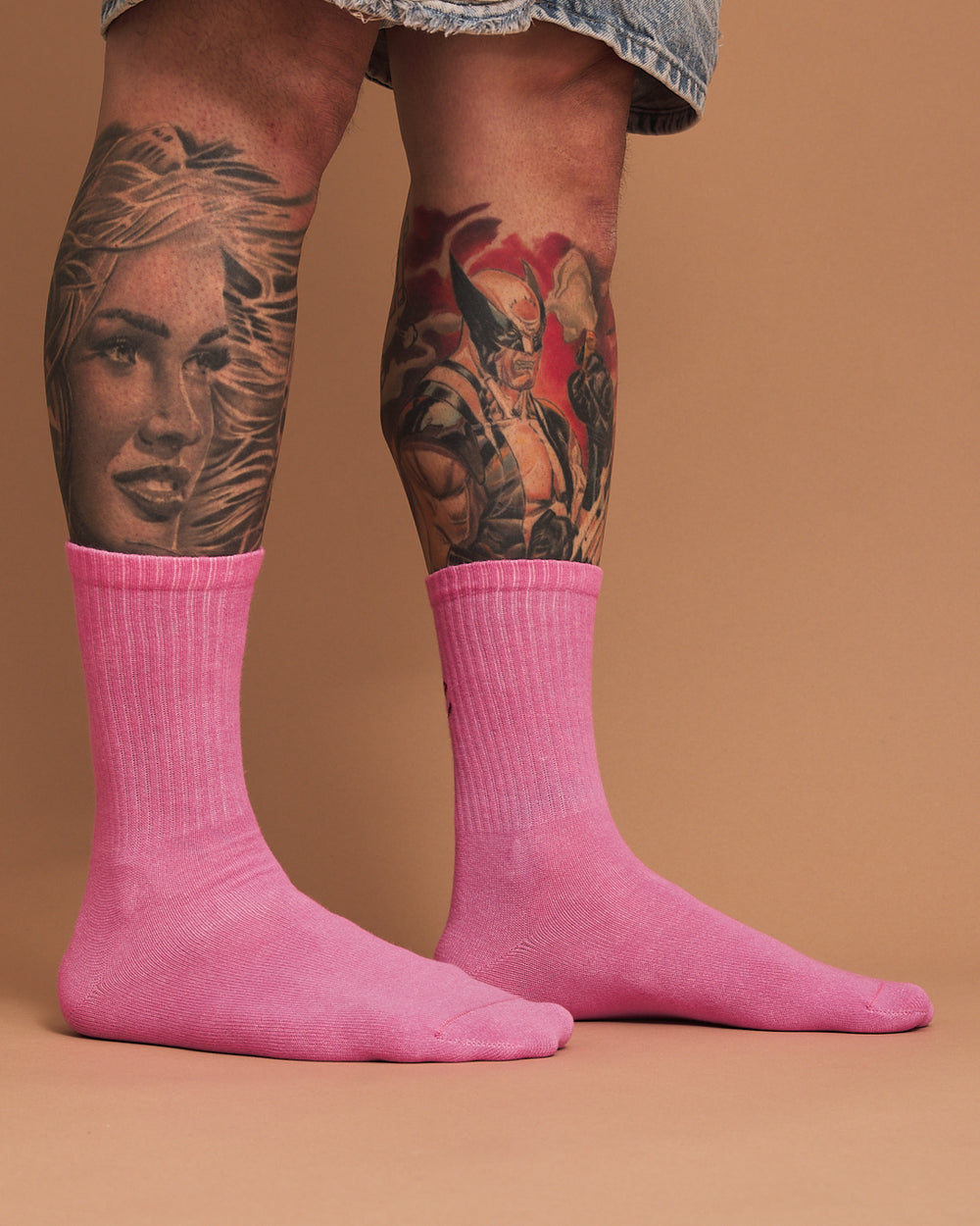 Person wearing pink socks with tattoos on a brown background