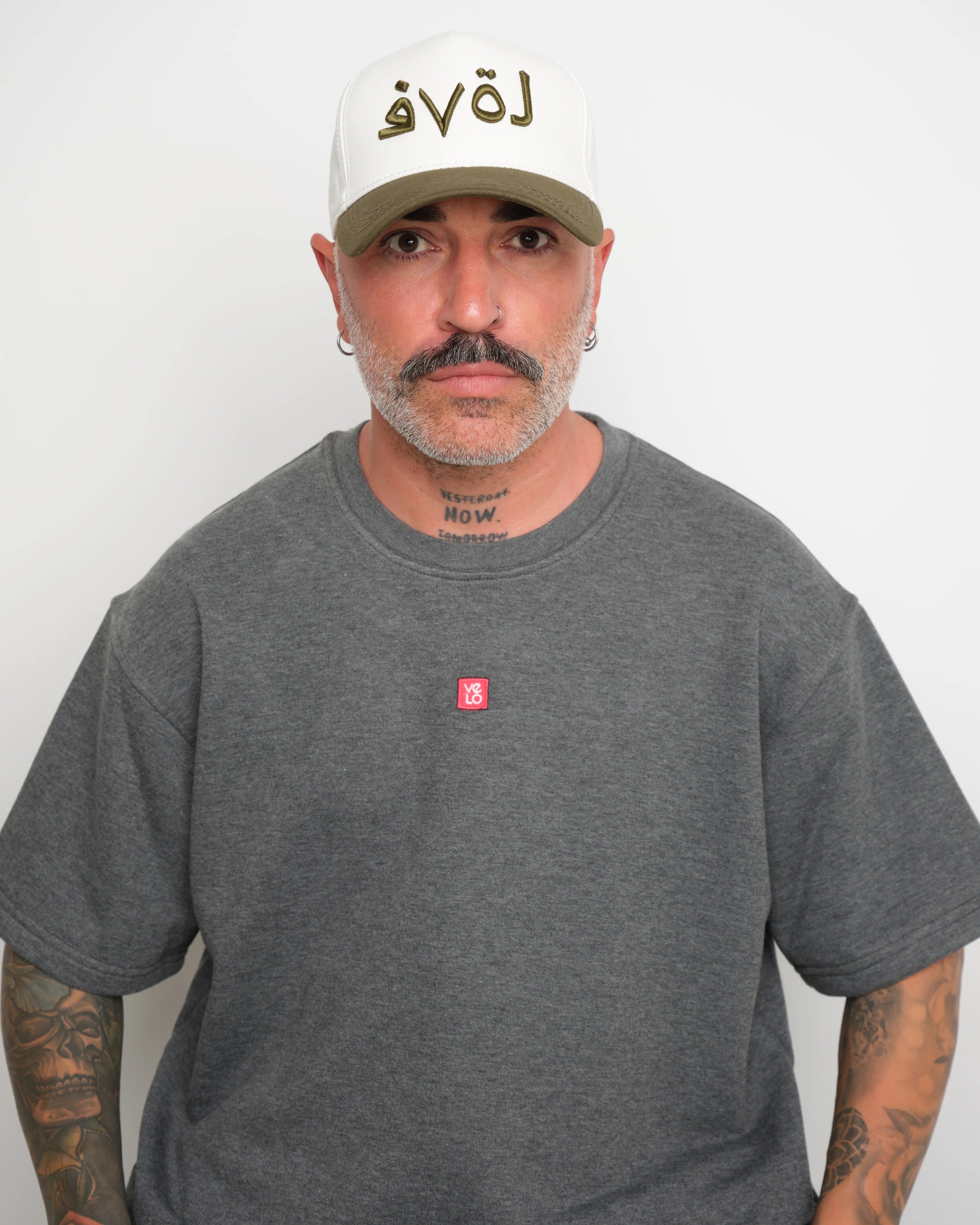 Man wearing a gray t-shirt with a small red logo and a white cap with khaki brim and  khaki 'love' text.