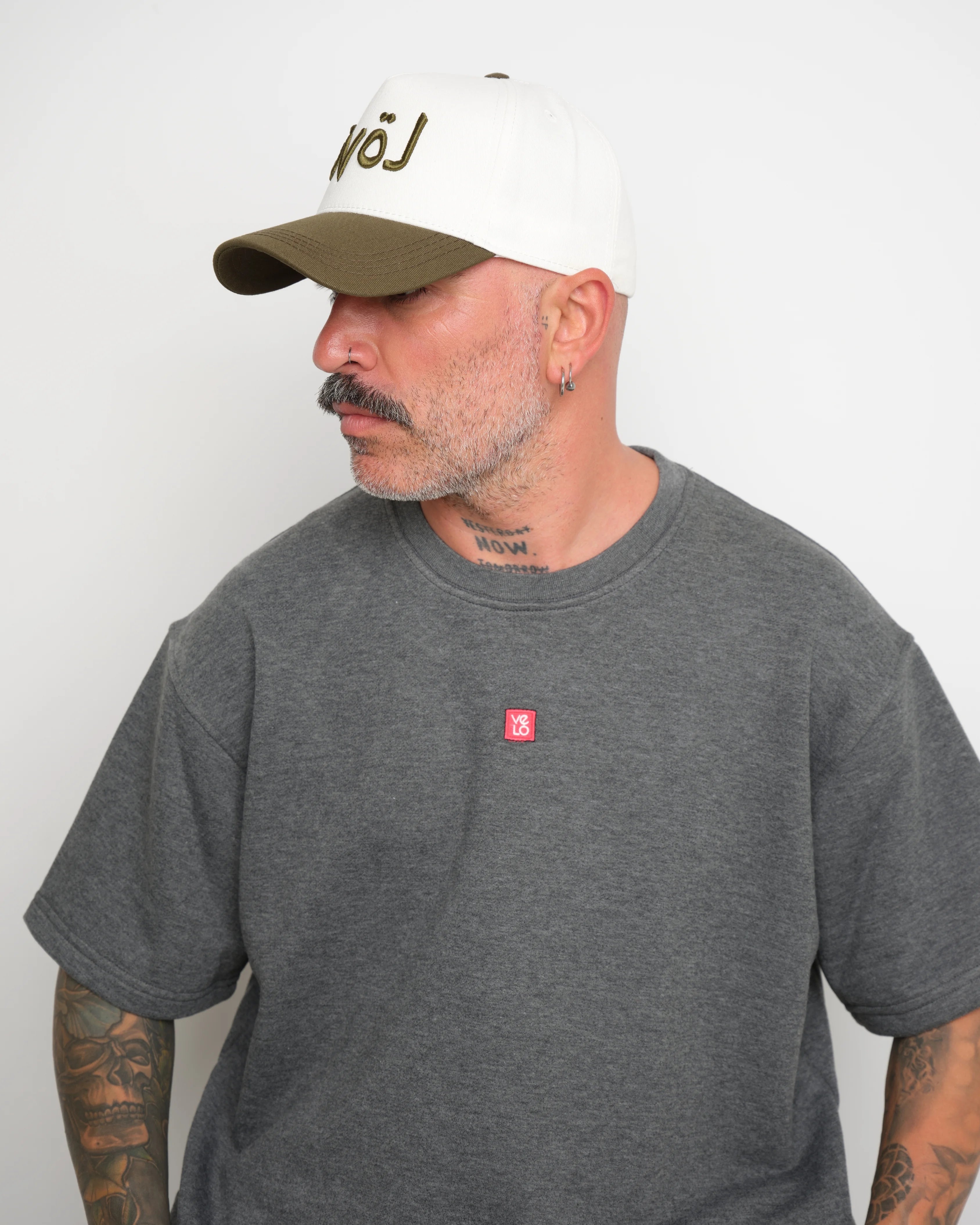 Man wearing a gray t-shirt with a red logo and a white cap with khaki 'love' lettering on a plain background