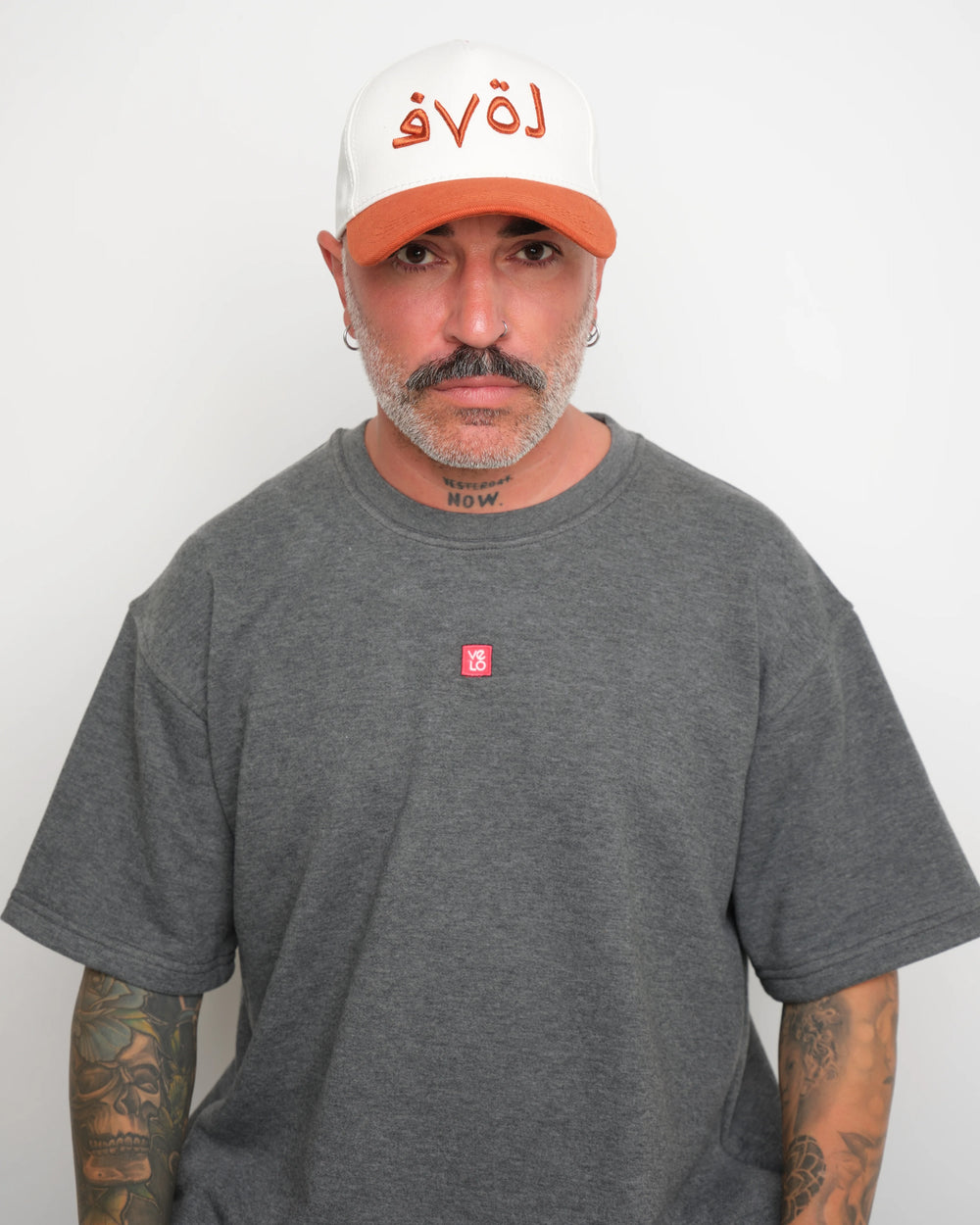 Man wearing a gray t-shirt and white cap with orange brim and 'love' text against a plain background