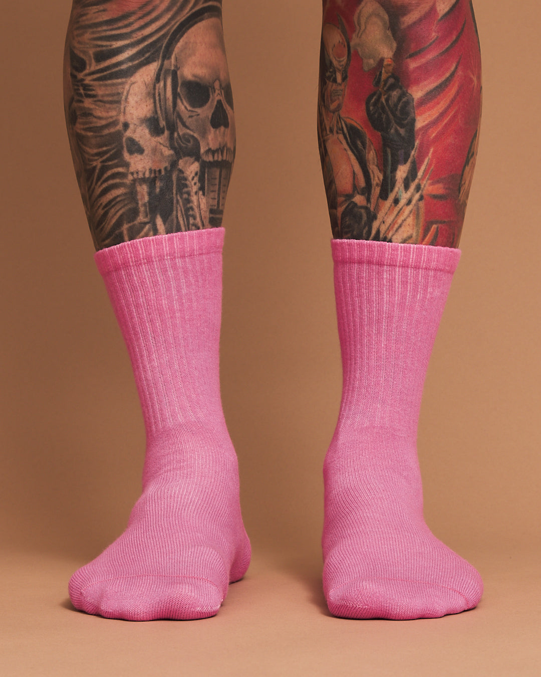 Person wearing pink socks with tattooed legs on a brown background