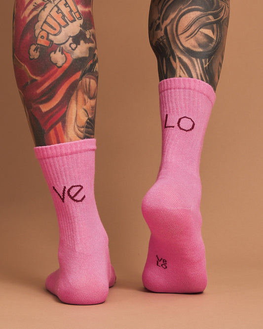 Pink socks with 'LOVE' text worn by a person with tattoos on a brown background