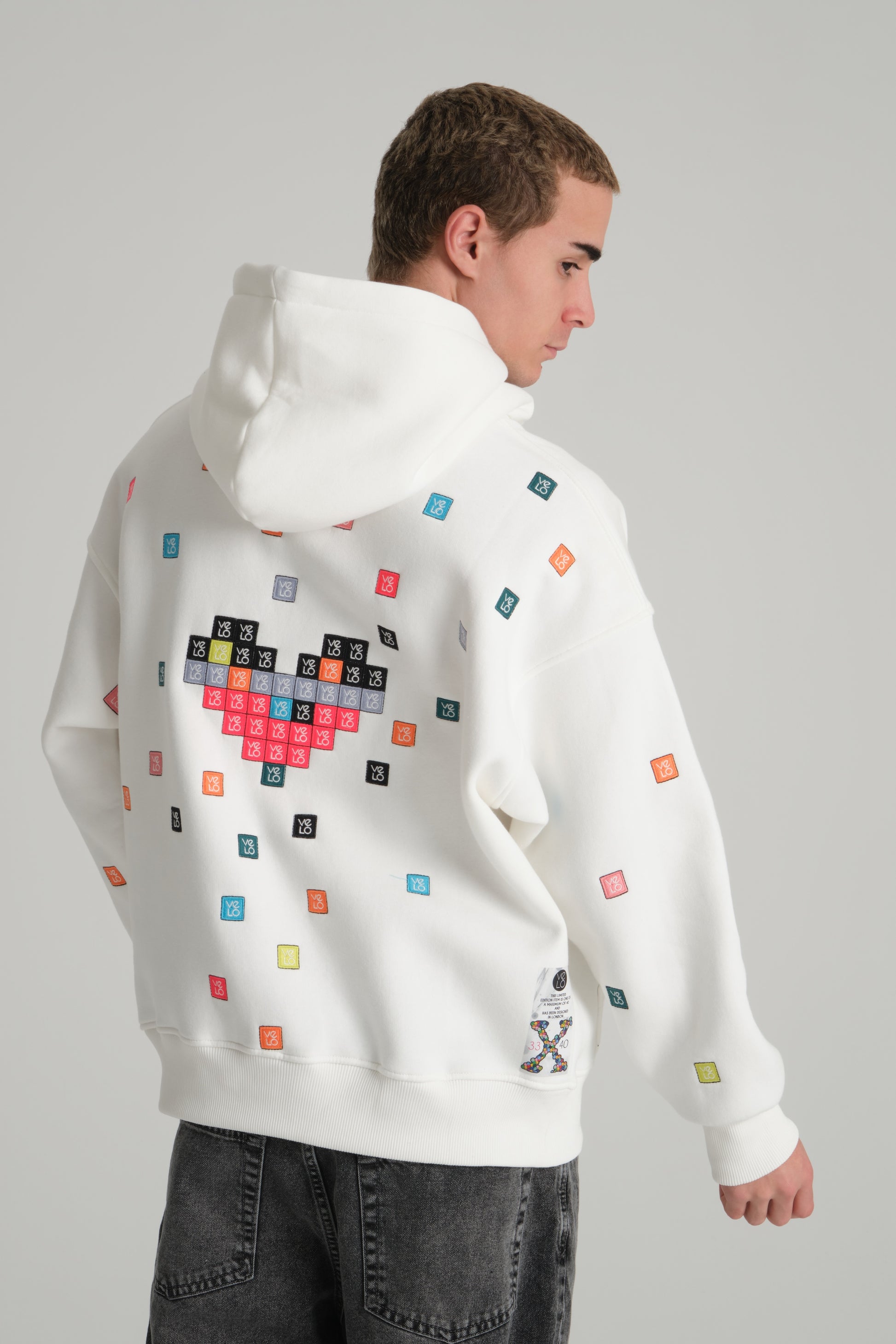 Person wearing a white hoodie with colorful pixelated design on the back against a gray background