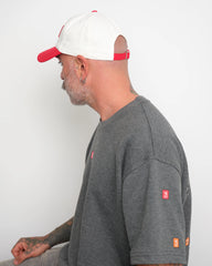Man wearing a gray t-shirt with 'velo' geometric stitched and showing flip tag of baseball cap on a white background