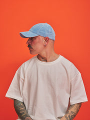 Person wearing a light blue cap and white t-shirt against an orange background