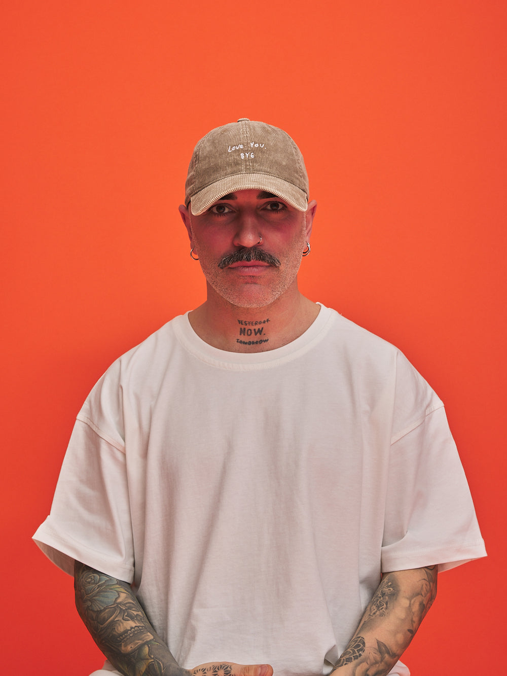 Person wearing a beige cap and white t-shirt against an orange background