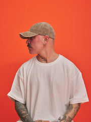 Person wearing a beige cap and white t-shirt against an orange background