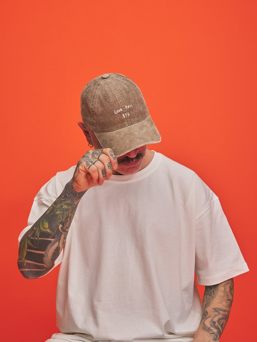 Person wearing a beige cap and white t-shirt against an orange background