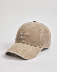 Beige corduroy cap with embroidered text on a light gray background