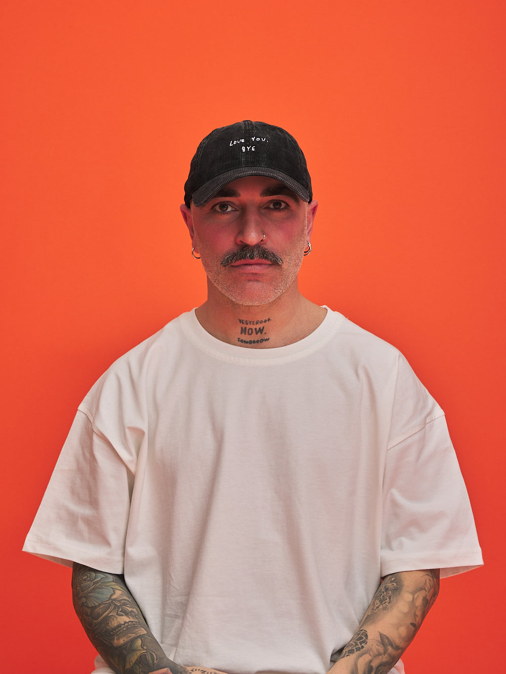 Person wearing a black cap and white t-shirt against an orange background