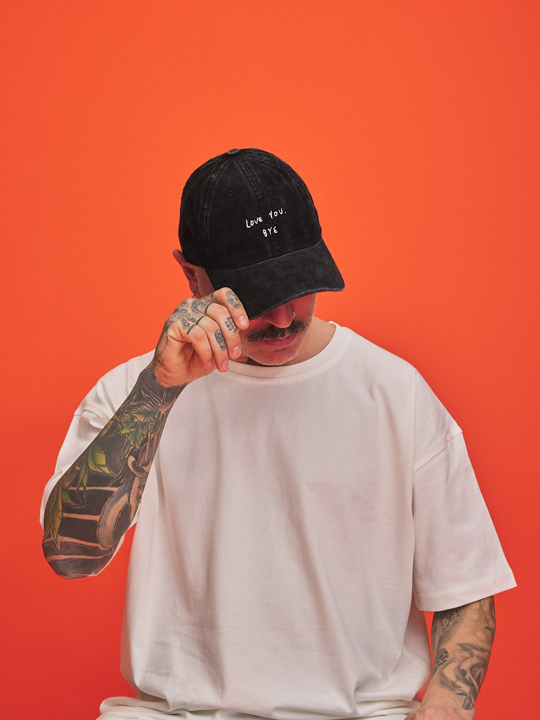 Person wearing a black cap with text and a white t-shirt against an orange background