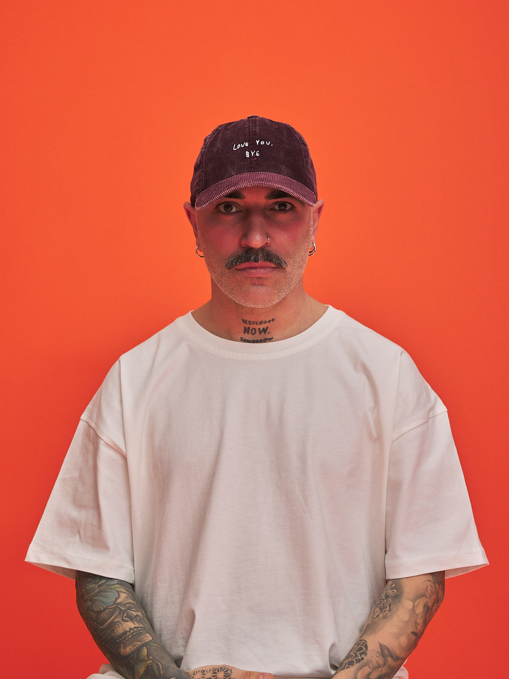 Person wearing a white t-shirt and burgundy cap against an orange background