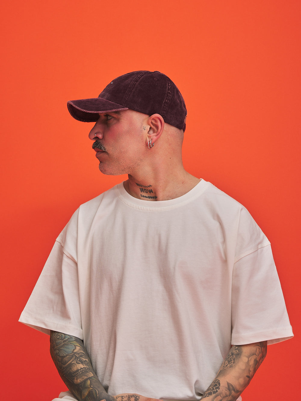 Person wearing a white t-shirt and burgundy corduroy cap against an orange background