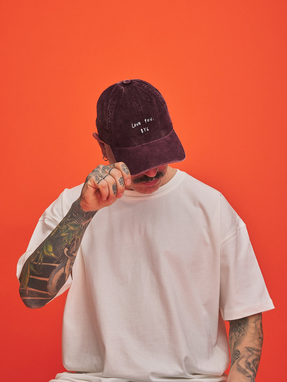 Person wearing a white t-shirt and burgundy cap with text on an orange background