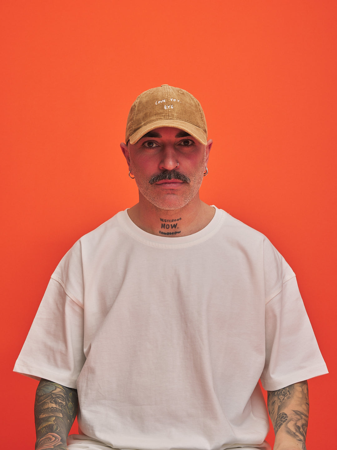 Man wearing a camel corduroy cap and white t-shirt against an orange background