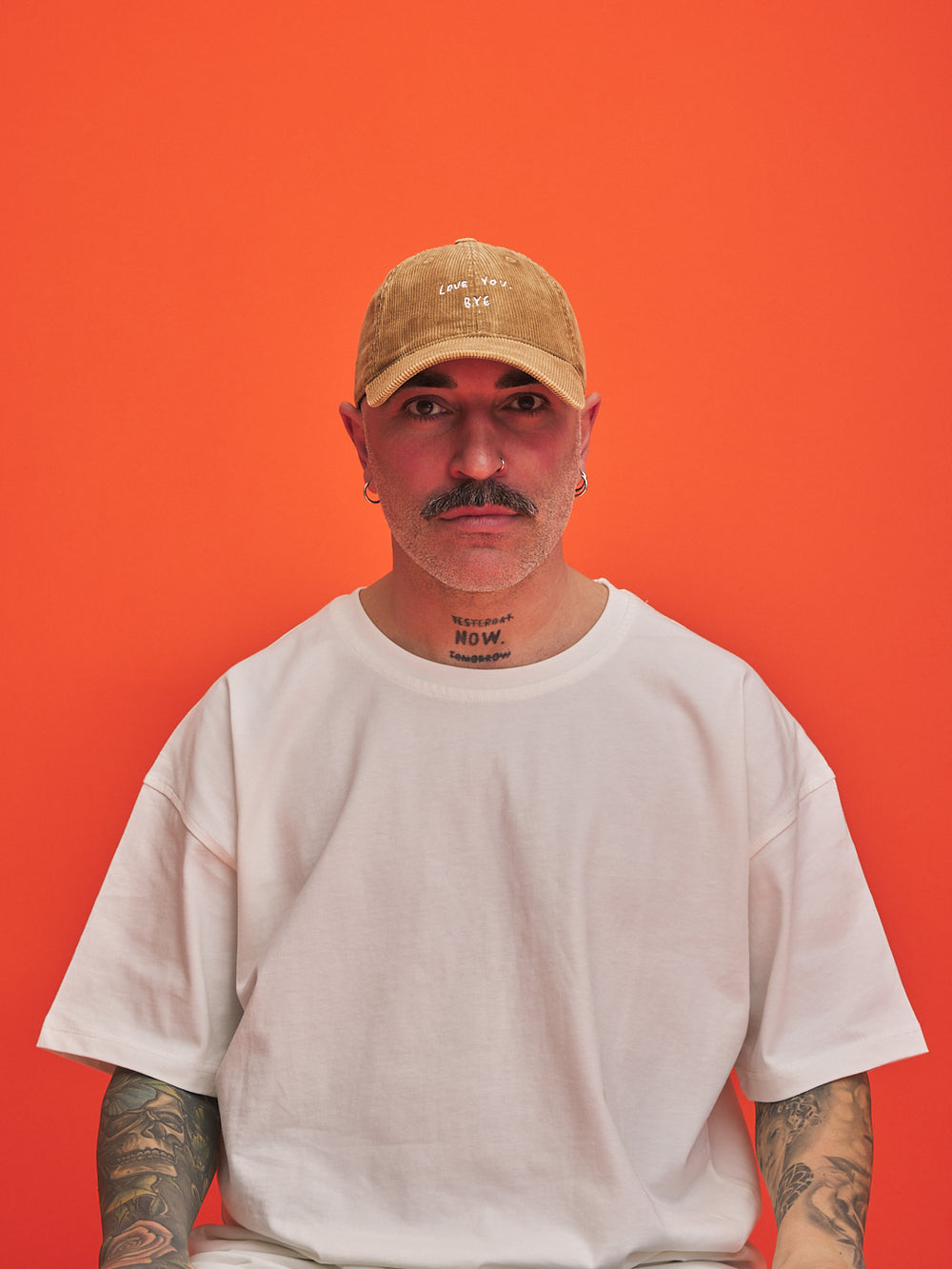 Man wearing a camel corduroy cap and white t-shirt against an orange background