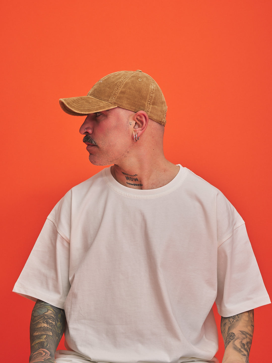 Person wearing a camel cap and white t-shirt against an orange background