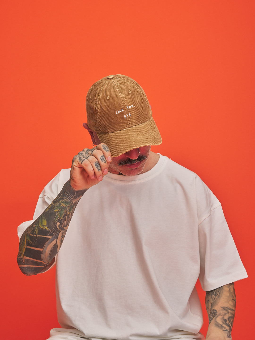 Person wearing a camel cap and white t-shirt against an orange background