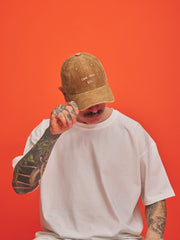 Person wearing a camel cap and white t-shirt against an orange background