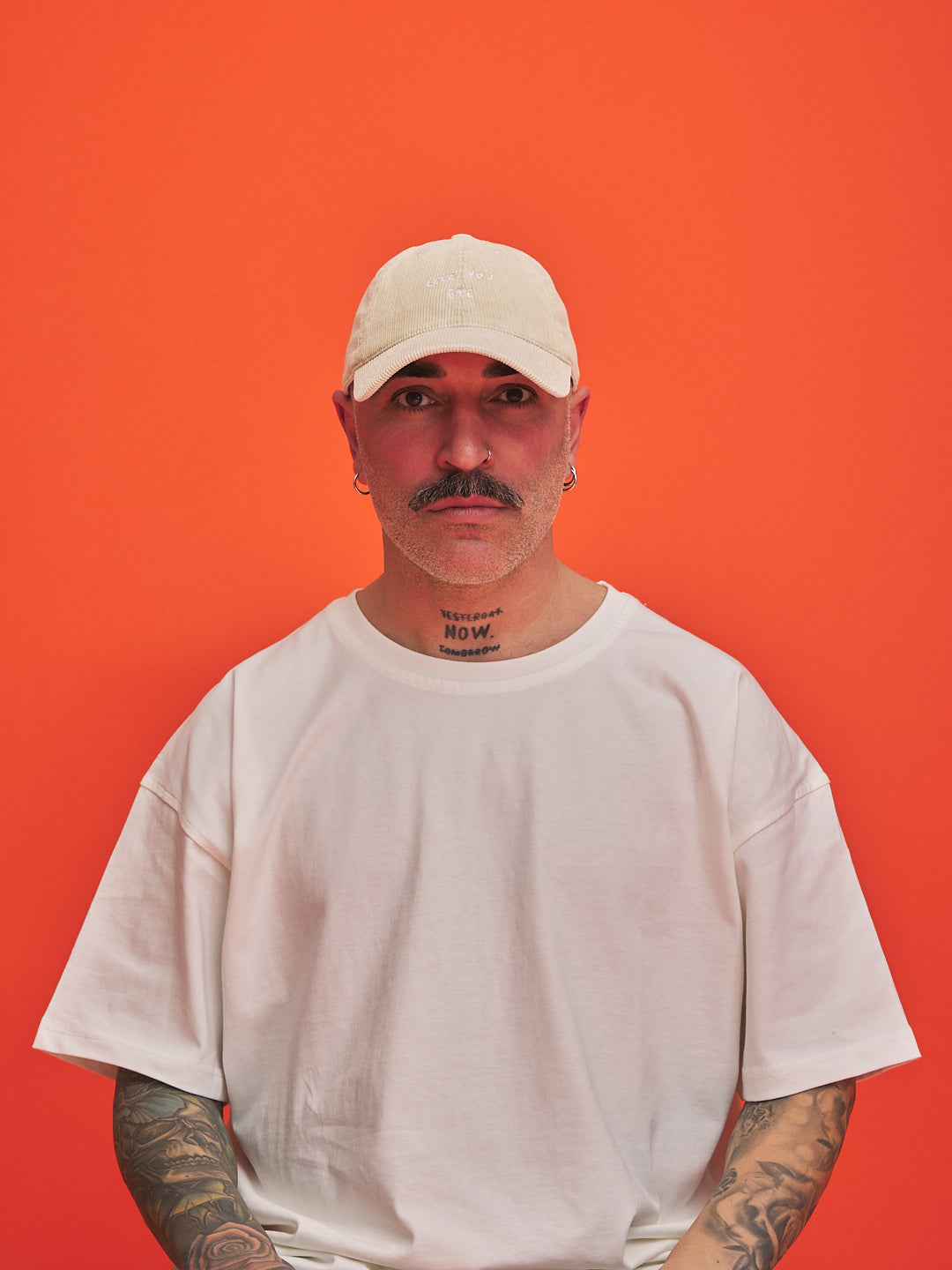 Person wearing a cream corduroy cap and t-shirt against an orange background