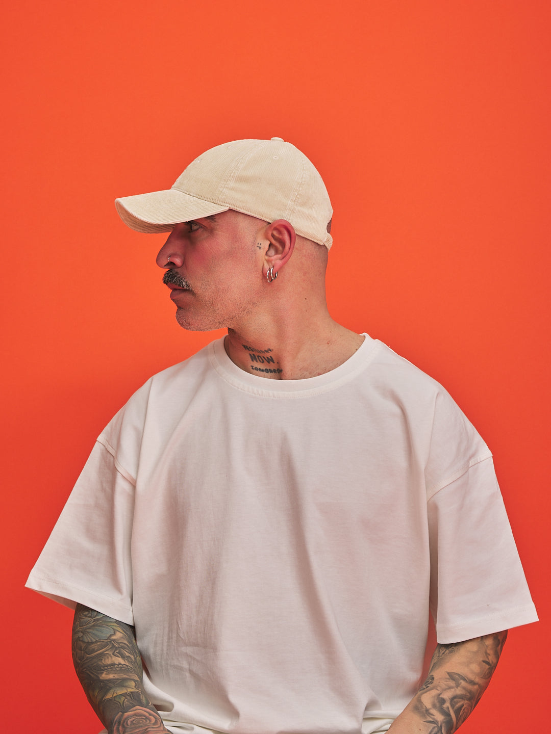 Person wearing a cream corduroy cap and white t-shirt against an orange background