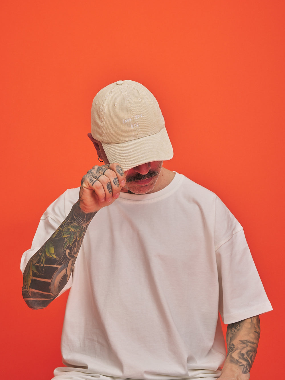 Person wearing a cream corduroy cap and white t-shirt against an orange background