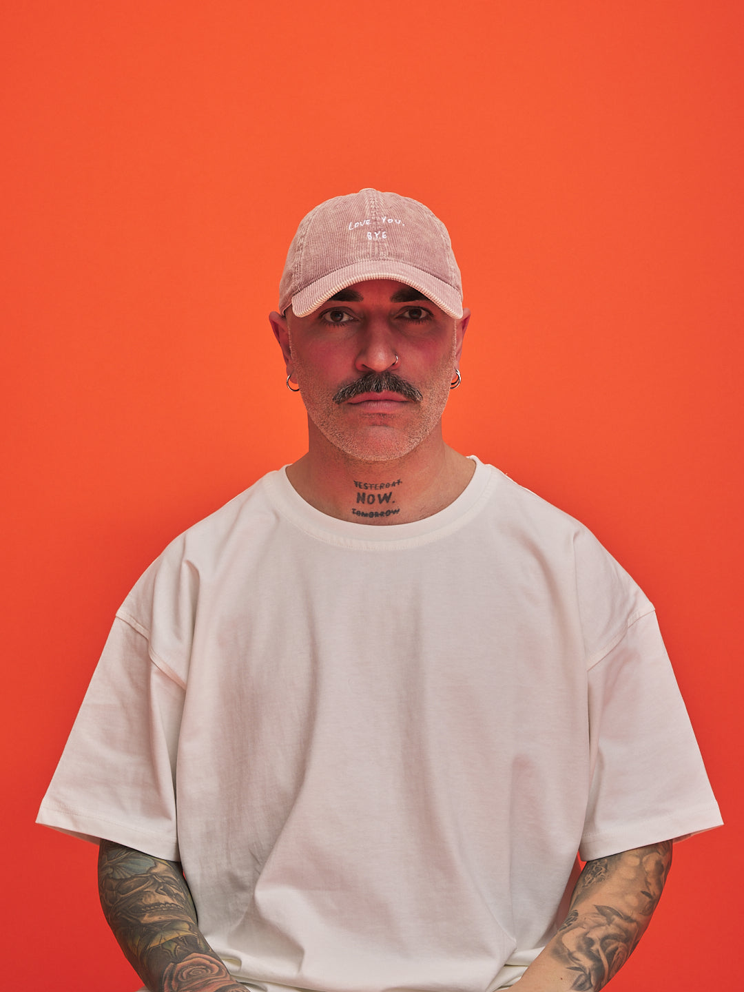 Man wearing a white t-shirt and pink cap against an orange background