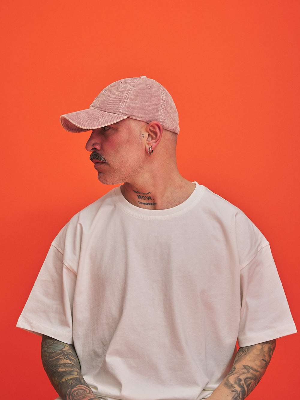 Person wearing a light pink cap and white t-shirt against an orange background