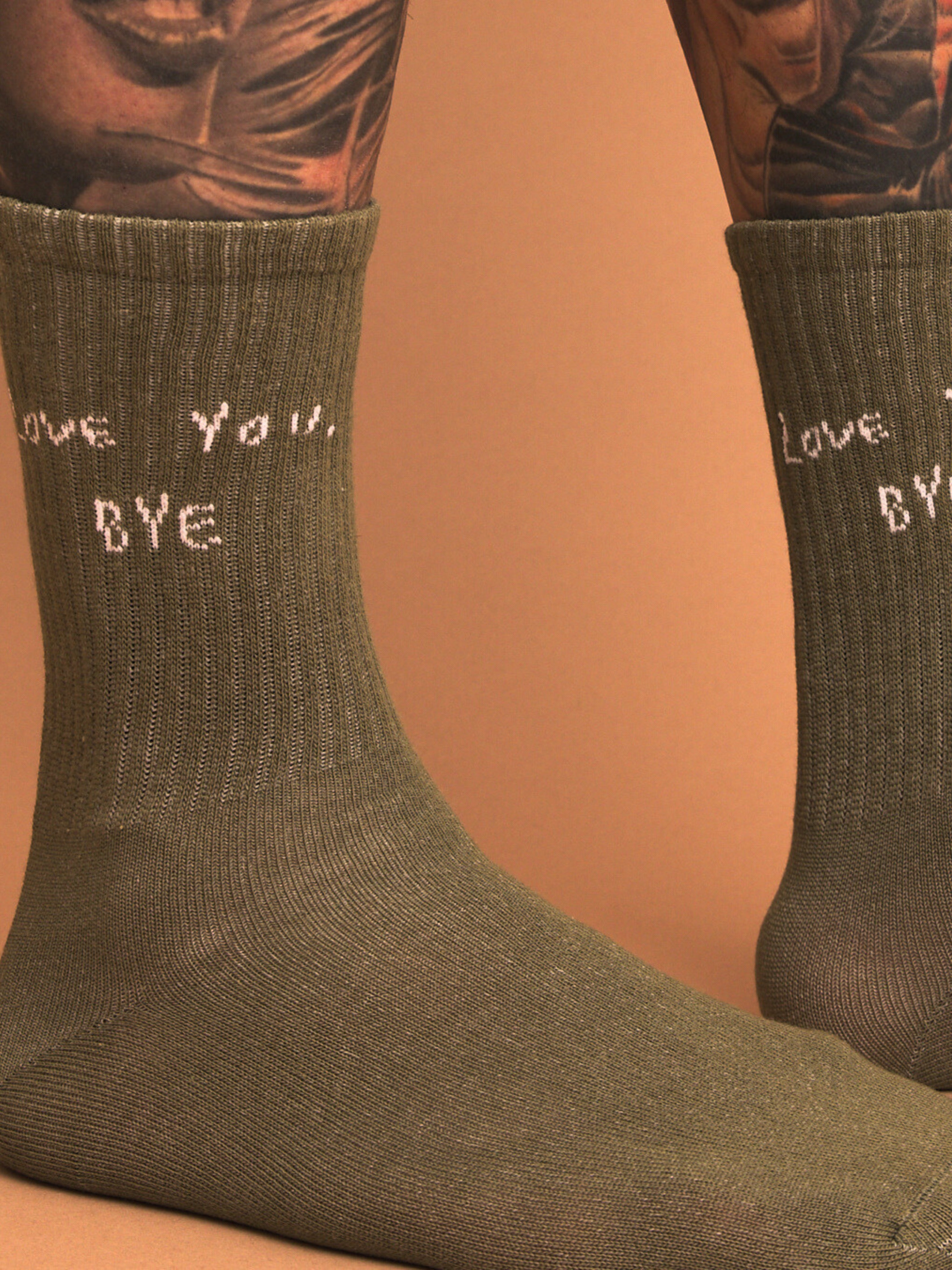 close up of khaki socks with text 'love you, BYE' worn by a person on a brown background