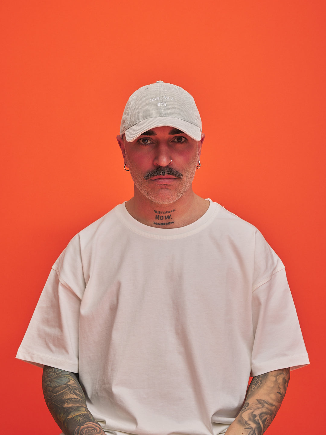 Person wearing a light grey corduroy cap and t-shirt against an orange background