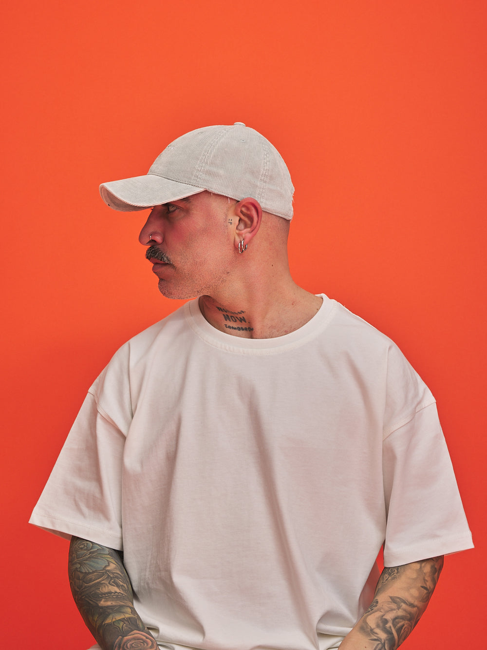 Person wearing a light grey corduroy cap and t-shirt against an orange background