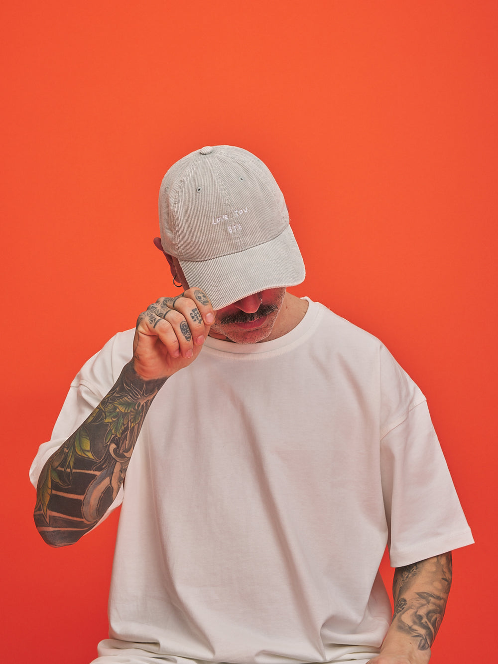 Person wearing a light grey corduroy cap and white t-shirt against an orange background