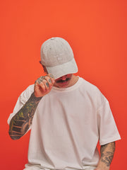 Person wearing a light grey corduroy cap and white t-shirt against an orange background