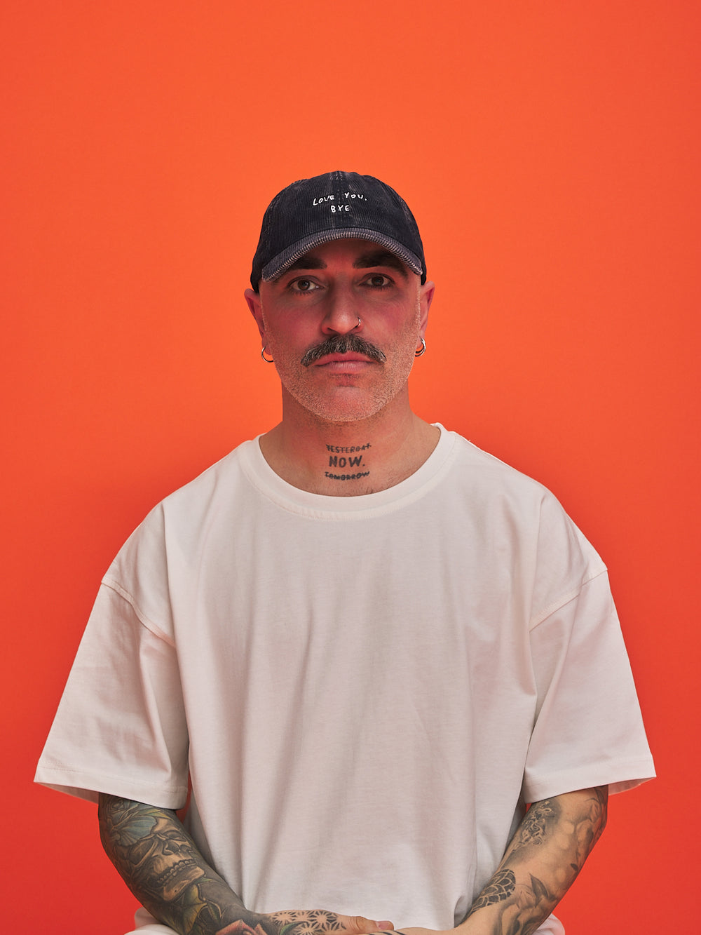 Man wearing a navy blue corduroy cap and white t-shirt against an orange background