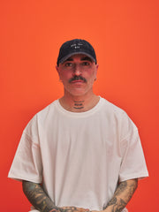 Man wearing a navy blue corduroy cap and white t-shirt against an orange background